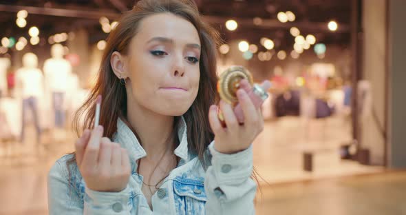 The Woman is Looking in a Small Mirror and Painting Her Lips with Lipstick alt