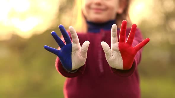Joyful Girl Waving Hands Painted in France Flag Colors and Say Hello Outdoor at Sunset alt