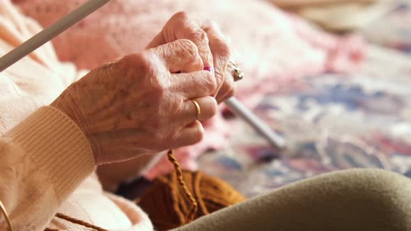 The grandmother is knitting on her sofa on a sunny morning, she squeezes the wool on the needle alt