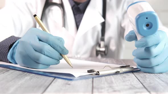 Hand Holding Infrared Thermometer and Writing on a Paper alt