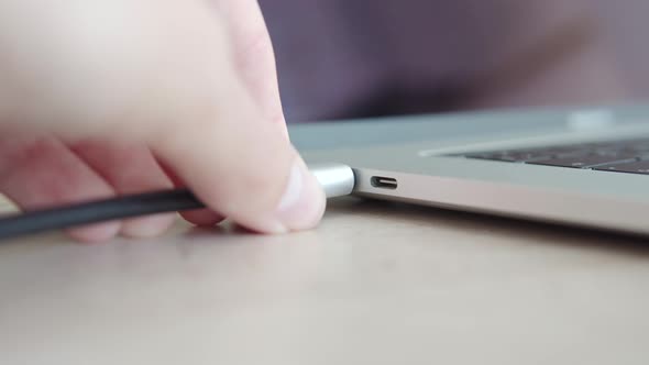 Hand Connects a USB Hub Cable or Charger Cable to a Modern Laptop Closeup