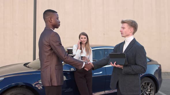Two Businessmen Greet Near the Office on the Background of a Sports Car alt