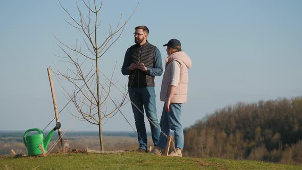 Couple of Volunteers Discussing Something While Standing Next to a Planted Tree alt