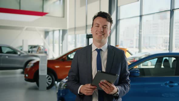 The General Manager of the Car Dealership in a Suit and Tie Smiles at the Camera alt