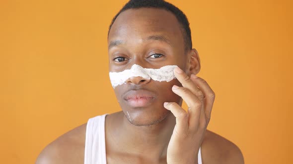 AfricanAmerican Man Applies Moisturizer To His Face Healthy Glowing Skin Isolated Yellow Background alt