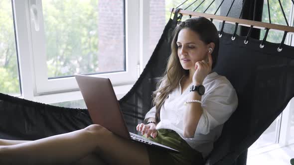 Woman Uses Video Chat on Laptop Lying in Hammock in Flat