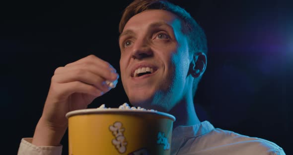Man watching a funny comedy movie at the cinema, he is laughing and eating popcorn