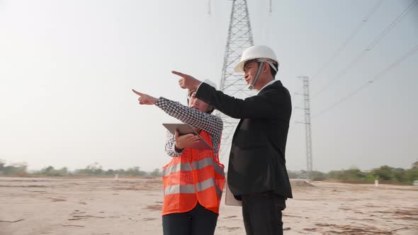 Engineer In Helmet Standing On Field With Electricity Towers. Teamwork, Leadership