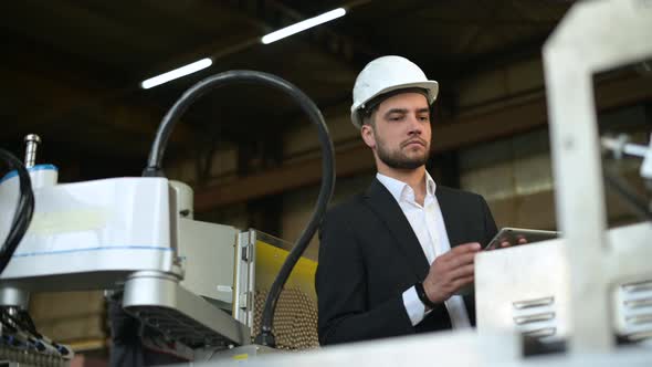 A young plant manager controls the machine's process and takes notes on a tablet alt