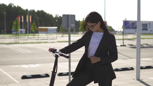 Business Woman Standing with Electric Scooter Wearing Black Suit alt