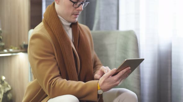 Serious Male in Elegant Suit Sit on Couch Working on Digital Tabletwearing Wireless Headphones