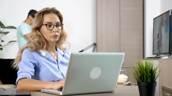 Tired and Streesed Woman Works on the Computer While Her Boyfriend Wears Virtual Reality Headset in alt