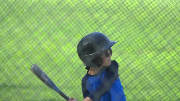 A boy hits a ball in a batting cage at little league baseball practice. alt