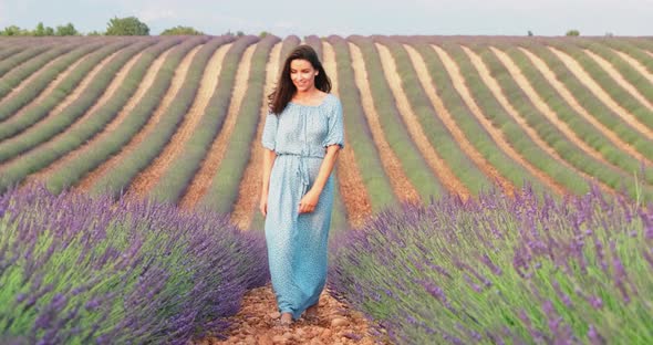 The Beautiful Young Girl Walks Across the Field of a Lavender at Sunset She is Wearing a Long Blue alt