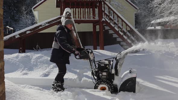 Man cleans snow on footpaths with snowblower.