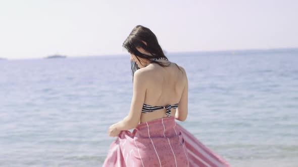 Woman in bikini wrapping towel around on beach