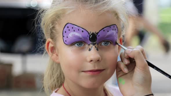 Children face painting. Artist painting little  girl like butterfly