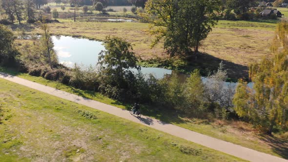Solitary biker riding through a landscape with grass fields and trees along the road with a river me alt
