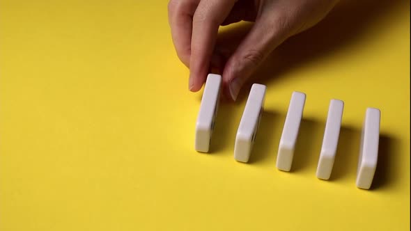 The hands of a young caucasian woman lay dominoes in a row.