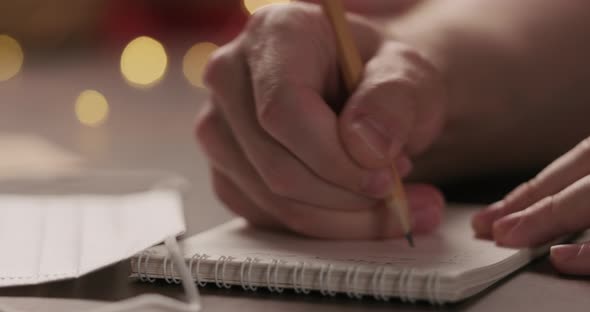 Slow Motion Closeup Man Writes Shopping List in Notepad with a Pencil Under Warm Light in the alt