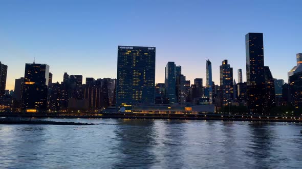 Camera glidinging over Hudson River with silhouetted skyline of New York City alt