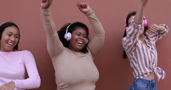 Happy latin girls having fun while dancing and listening music playlist with headphones alt