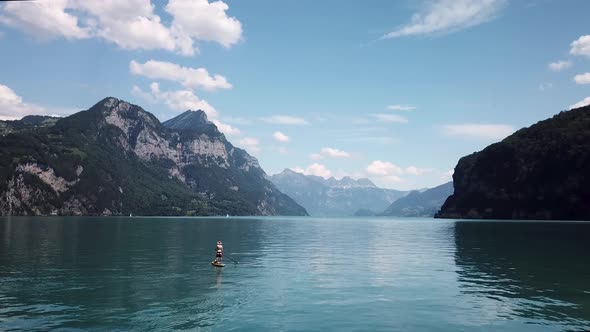 Orbiting aerial shot around a stand up paddler on a yellow stand up paddle, sup with a straw hat in alt