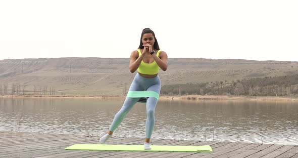 Young smiling fitness woman doing fitness exercises on lake. alt