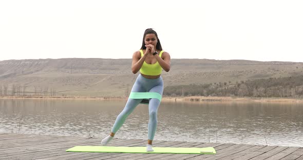 Young smiling fitness woman doing fitness exercises on lake.