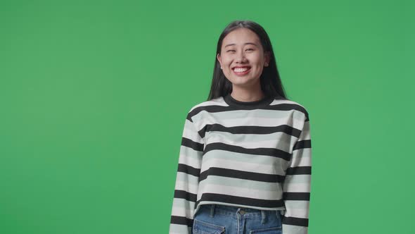 A Smiling Asian Woman Dabbing While Standing In Front Of Green Screen Background alt