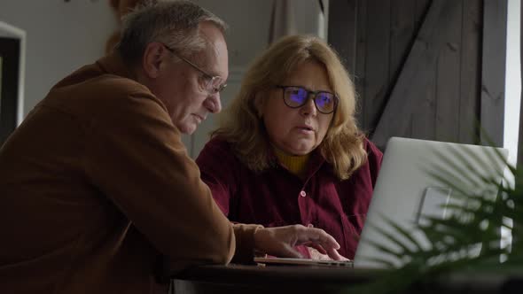 two elderly people surfing internet on laptop computer at home. alt