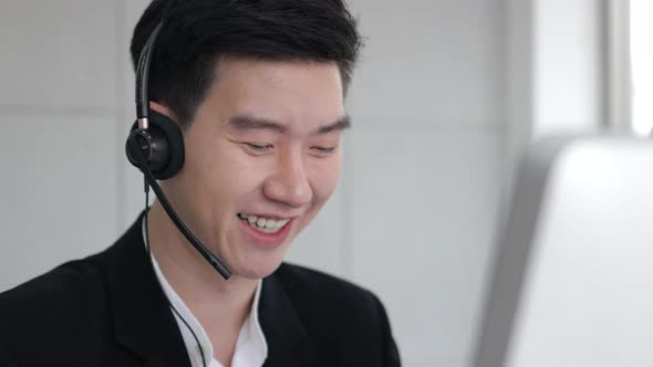Asain call center wear headset and working with computer while consulting customer alt