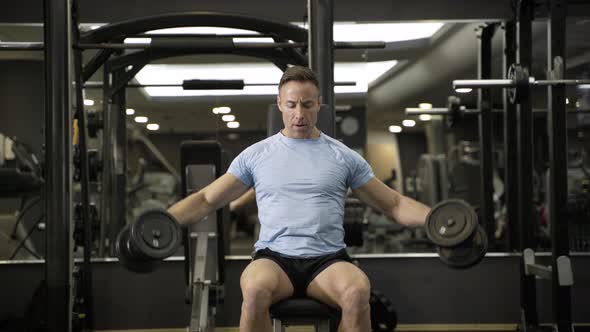 Muscular man holding dumbbell above the head at the gym. alt