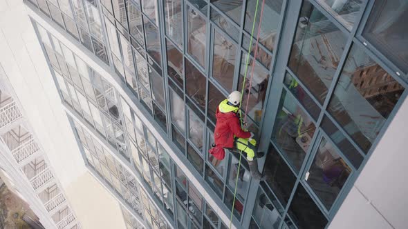 Climber in Overall and Helmet Washes Windows of Skyscraper alt