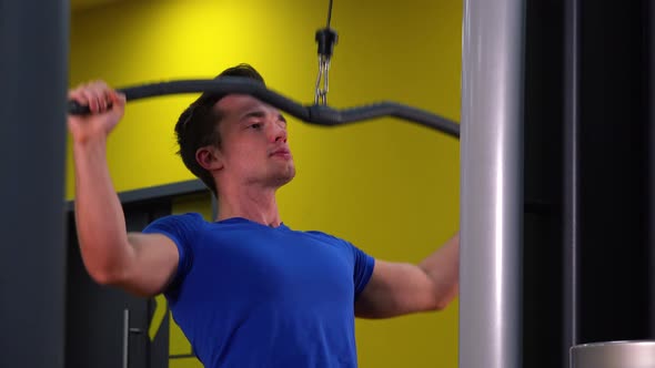 A Young Fit Man Trains on a Cable Tower in a Gym alt