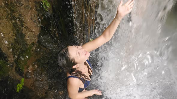 A Beautiful Asian Girl is Smiling Happily with Happiness Touching a Powerful Waterfall Stream in