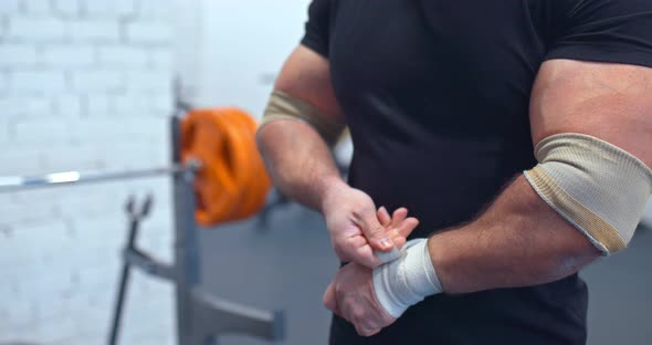 Heavyweight Man Wraps His Wrists with Elastic Bandages Preparing for Sports alt