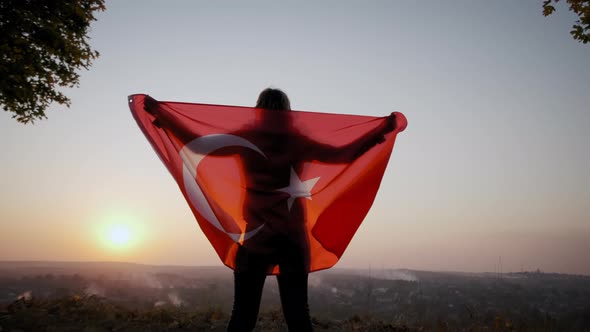 Back View of Happy Woman with Turkish National Flag Standing Outdoors at Sunset alt