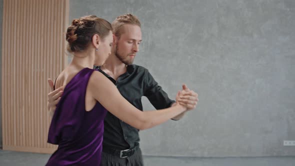 Man and Woman are Actively Dancing a Tango in Gray Room with Large Windows