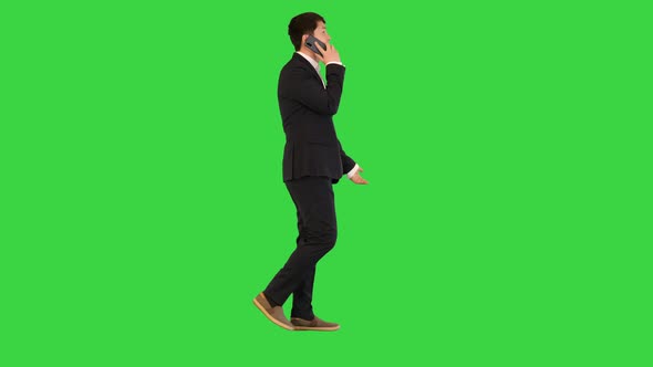 Asian Businessman Walks Talking on Mobile Phone on a Green Screen Chroma Key alt