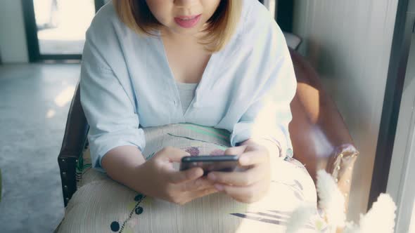 Asian woman using smartphone for talking, reading and texting while sitting on table in cafe. alt