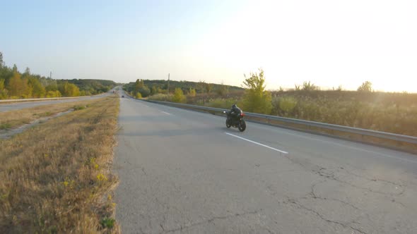 Biker Riding on Modern Sport Motorbike at Highway During Sunny Autumn Day alt