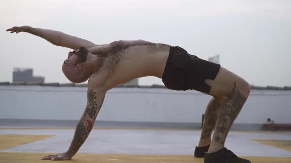 Male Performs Back Bend Yoga Exercise With Both Feet And One Hand On The Ground alt