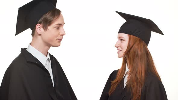 Ginger Caucasian Graduate Female Talking with Male in Black Robe and Square Academical Cap on White alt