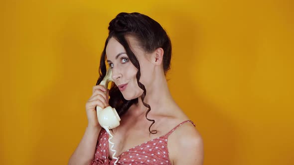 An attractive female model on a orange background wearing a vintage dress talking on the phone