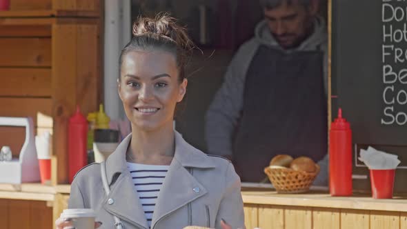 Smiling woman standing with coffee near food booth