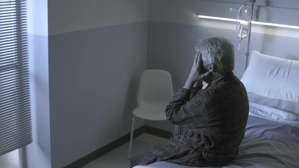 Sad hopeless senior sitting in a hospital bed alone