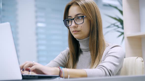 Cute Woman Working at a Laptop with Glasses Typing Text in the Office Employee at Work on the alt
