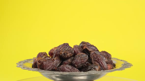 dried large dates on a metal plate that rotates, yellow background