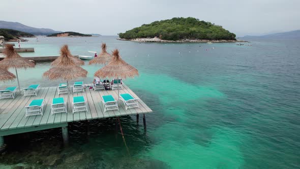 Aerial View of Empty Sunbeds Under Thatched Umbrellas on a Pier in Turquoise Sea alt